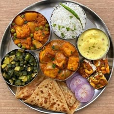 a metal plate filled with different types of food on top of a wooden table next to rice