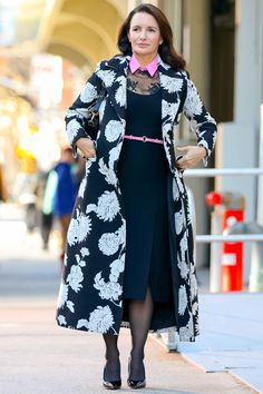 a woman is walking down the street wearing a black and white coat with flowers on it