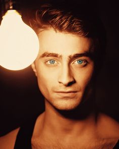 a man with blue eyes standing in front of a light bulb and looking at the camera