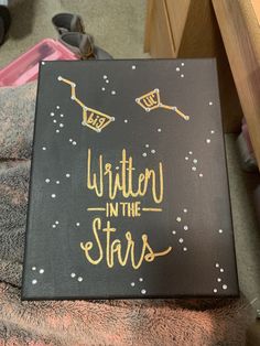 a sign that says written in the stars on top of a black box with gold lettering