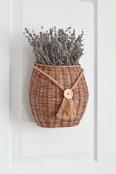 a wicker basket hanging on the wall with lavenders in it and a wooden button