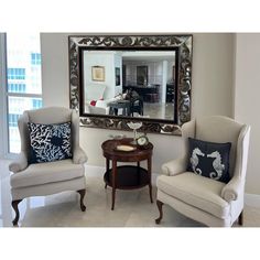 a living room with two chairs and a table in front of a large framed mirror