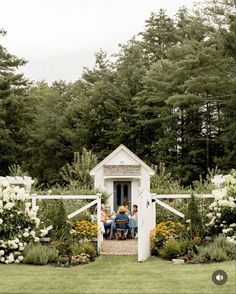 three people sitting on a bench in the middle of a garden with white flowers and greenery