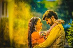 a man and woman hugging each other in front of yellow powder pouring from the air