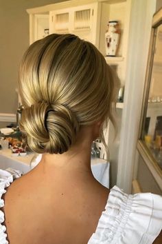 a woman with blonde hair in a low bun hairstyle looking at herself in the mirror