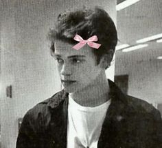 a black and white photo of a young man with a pink bow on his head