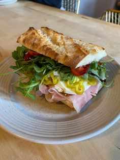 a sandwich with meat, lettuce and tomato on a plate at a table