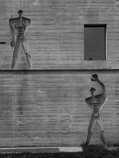 black and white photograph of two sculptures on the side of a building, one holding a baseball bat