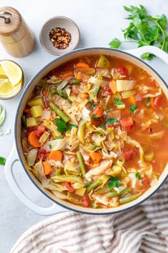 a pot filled with vegetable soup next to sliced lemons and parsley on the side