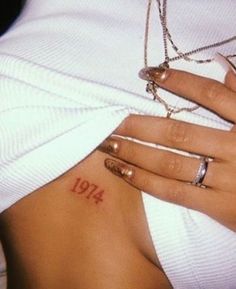 a woman's stomach with a small tattoo on her left side and the number 1974 written in red ink