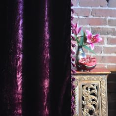 a vase with flowers sitting on top of a table next to a purple velvet curtain