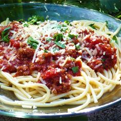 spaghetti with sauce and parmesan cheese in a glass bowl on top of a table