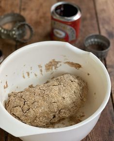 a bowl filled with food sitting on top of a wooden table next to cans of soda