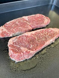 two raw steaks cooking in a frying pan