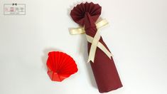 an origami fan next to a folded red paper flower on a white surface