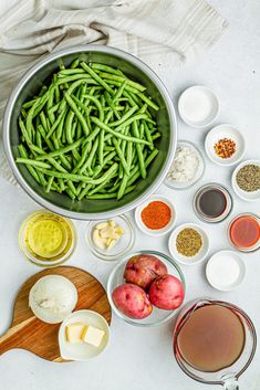 green beans, onions, garlic, and other ingredients are arranged in bowls on a white surface