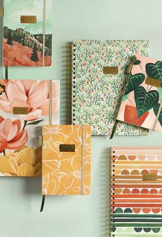 four notebooks are lined up on a wall with flowers and leaves in the pages