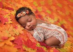 a baby is sleeping on some colorful leaves with her head tucked under her arms and eyes closed