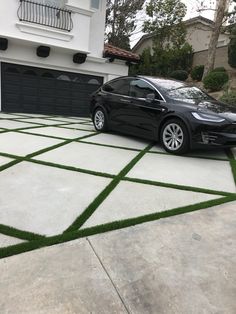 a black car parked in front of a house with grass growing on the driveway area