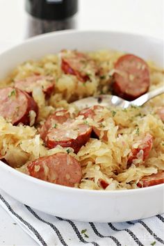 a white bowl filled with sausage and sauerkraut next to a bottle of wine