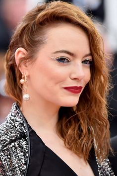 a woman with red hair and blue eyes is smiling at the camera while wearing earrings