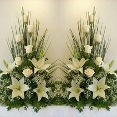 two vases with white flowers and greenery on top of a table in front of a mirror