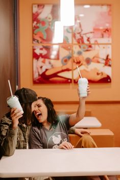 two people sitting at a table with cups in their hands and one holding a straw