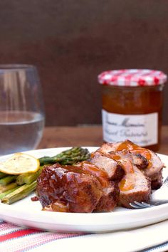 a white plate topped with meat and asparagus next to a glass of wine