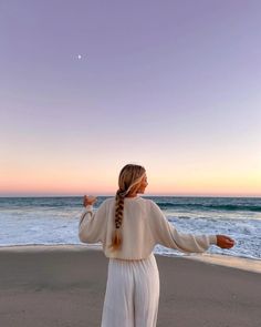 a woman standing on top of a sandy beach next to the ocean with her arms outstretched