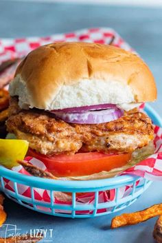 a fried chicken sandwich on a bun with onions and tomatoes in a basket next to fries