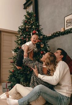 a family is sitting on the floor in front of a christmas tree and smiling at each other