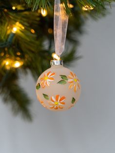 an ornament hanging from a christmas tree decorated with orange and yellow flowers on it