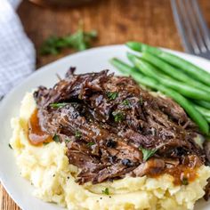 a white plate topped with mashed potatoes covered in meat and gravy next to green beans