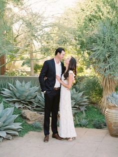 a man and woman standing next to each other in front of some cactus plants at their wedding