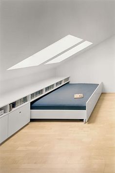 a bed sitting under a window in a room next to a book shelf and cupboards