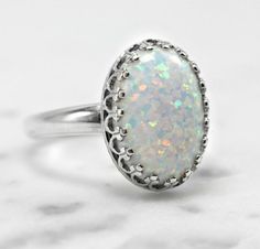 "This gorgeous white pinfire opal sits in a sterling silver 14 x 10mm (9/16\" x 3/8\") crown ring bezel that comes in 6, 7, 8, and 9 US ring sizes. The opal is lab-created with tones of sparkle in shades of pink, blue, lavender and green. Please read more about lab-created opals below. Opals are the birthstone of October but they are also known as the gem of choice by most and loved by many. If you have any questions please do not hesitate to contact me. What is a lab-created opal... Lab-created Oval Cabochon White Gold Opal Ring, Oval Cabochon Opal Ring In White Gold, Oval White Gold Opal Cabochon Ring, Classic White Opal Ring With Birthstone, Classic White Opal Birthstone Ring, White Opal Ring As A Gift, White Opal Ring For A Gift, Classic White Round Opal Ring, Elegant White Opal Birthstone Ring