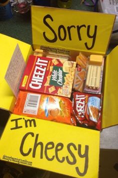 a person holding up a yellow box filled with snacks and candy that reads sorry, i'm cheesy