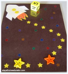 a paper board with stars and a rocket ship on it, next to a dice that says space