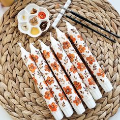 four white chopsticks with orange flowers on them next to some dipping sauces