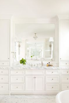 a large bathroom with white cabinets and marble counter tops, along with an oval bathtub