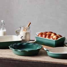 green dishes and bowls on a wooden table with milk in a glass bottle, salt shaker, cinnamon buns