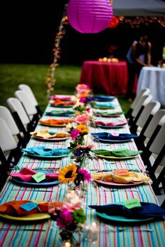 a long table is set with colorful plates and place settings for an outdoor dinner party