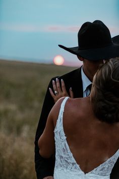 a bride and groom standing in the middle of an open field at sunset or sunrise