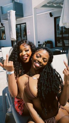 two young women sitting on top of a beach chair posing for the camera with their arms around each other