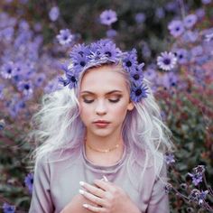 a woman with white hair and blue flowers in her hair is looking down at her hands