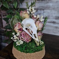 a flower arrangement with flowers and an animal's skull in it on a wooden table