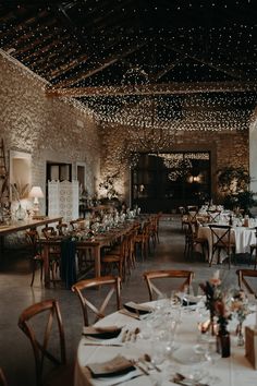 a dining room with tables and chairs covered in white tablecloths, lights strung from the ceiling