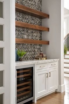 a wine cellar built into the side of a wall in a kitchen with white cabinets and wooden shelves