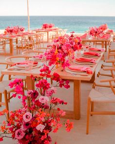 a table set up with pink flowers and place settings for an outdoor dinner on the beach