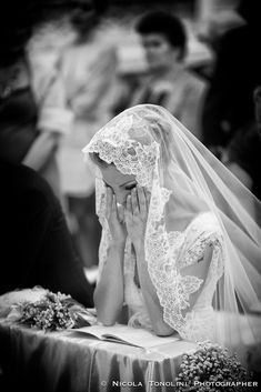 a woman sitting at a table with a veil on her head and holding her hands to her face